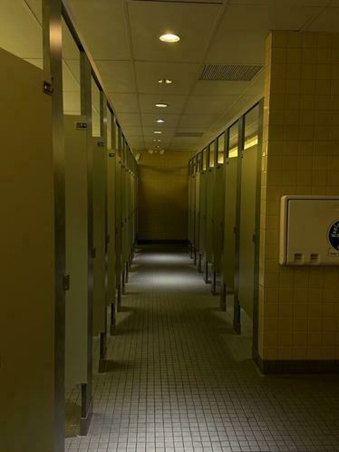 Long row of empty bathroom stalls stretching into the distance, a haunting liminal space.
