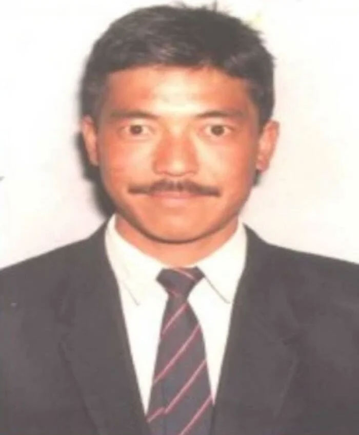 A portrait of a man with a mustache in a suit and tie, identified as the frozen body known as Green Boots on Mount Everest.