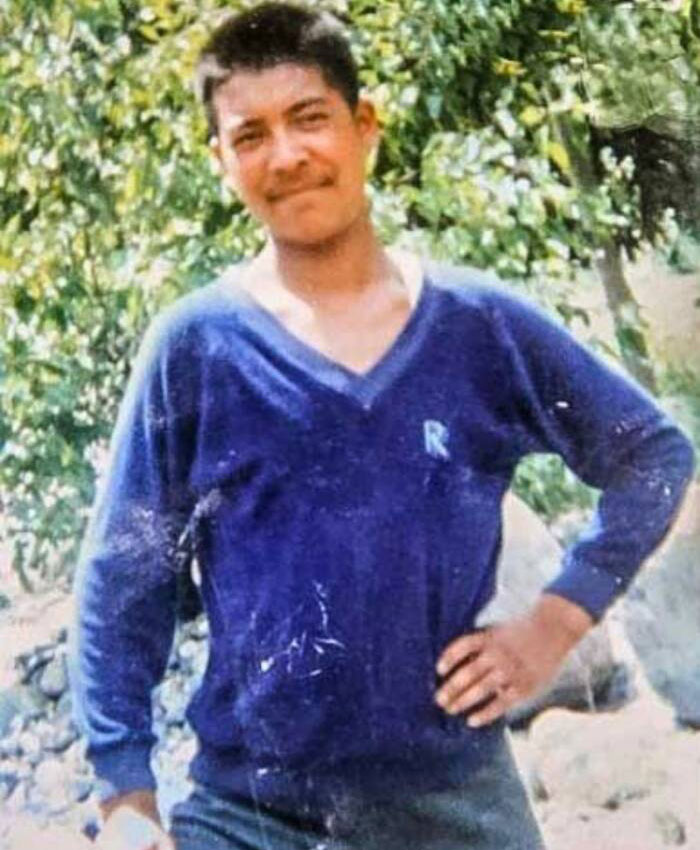A younger man, identified as the frozen body known as Green Boots on Mount Everest, smiling outdoors in a blue V-neck sweater.
