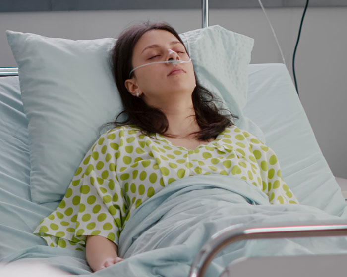 Woman with oxygen tube resting in hospital bed due to back injury