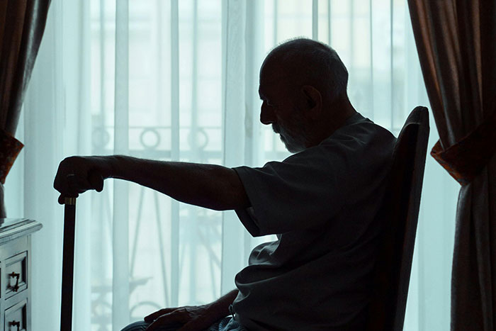 Silhouette of elderly man sitting with cane in dimly lit room