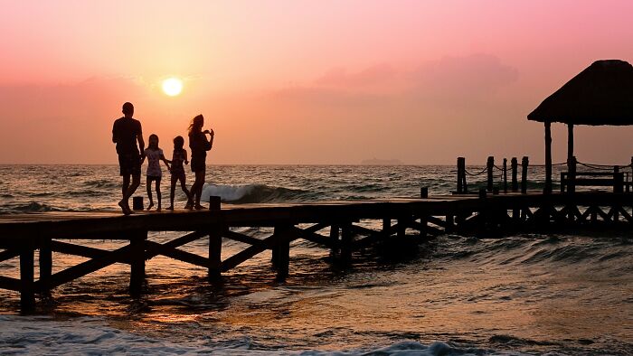 Family walking on wooden pier at sunset by the ocean