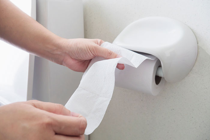 Hands pulling toilet paper from dispenser highlighting unhygienic habits
