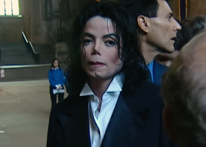 Michael Jackson in a black suit and white shirt, appearing serious during a public event