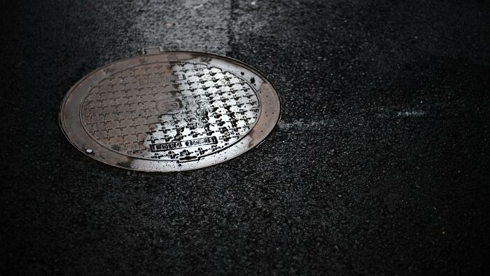 Wet manhole cover on street reflecting light related to moral dilemmas