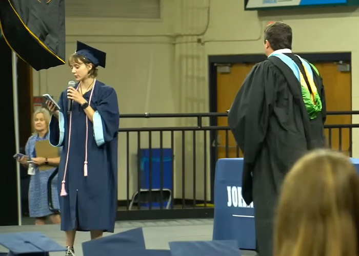 Female HS valedictorian speaking at graduation ceremony with faculty nearby Female HS valedictorian speaking at graduation ceremony with faculty nearby