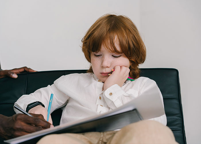 A child with red hair concentrating while drawing, symbolizing new research on autism and understanding the condition. A child with red hair concentrating while drawing, symbolizing new research on autism and understanding the condition.