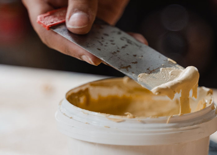 A hand using a putty knife to spread filler from a container, a practical solution to problems.