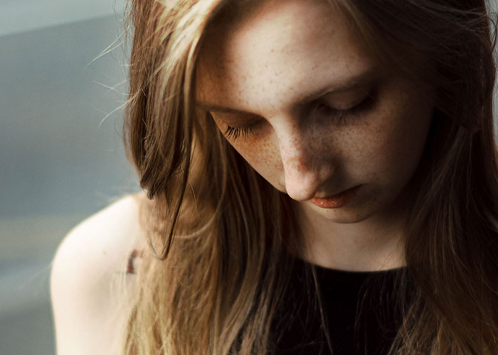A young woman with long hair and freckles looks down sadly, understanding kids can't keep contact with parents.
