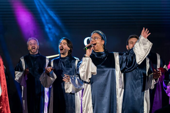 Singers in dark blue robes with white satin trim, performing on a stage with purple and blue lights. Craziest plane interactions.