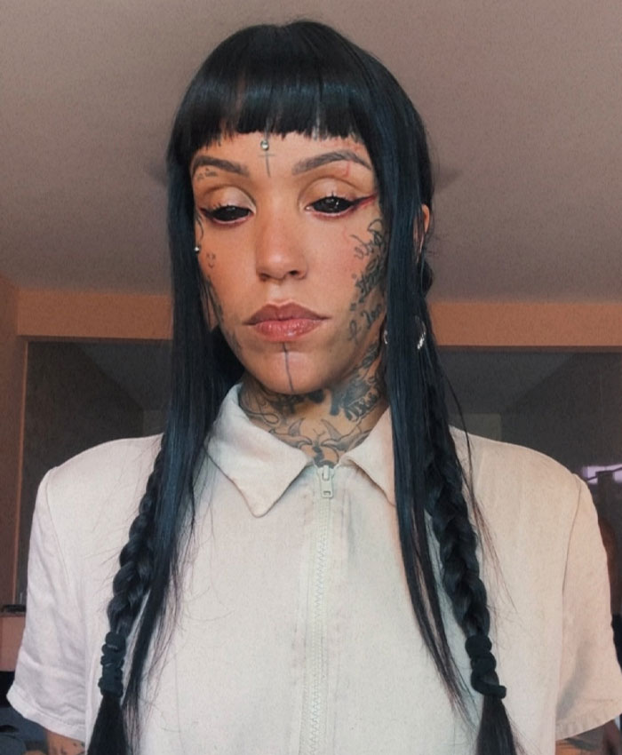 Woman with tattooed eyes, dark hair, and subtle makeup, showcasing her tattoos.