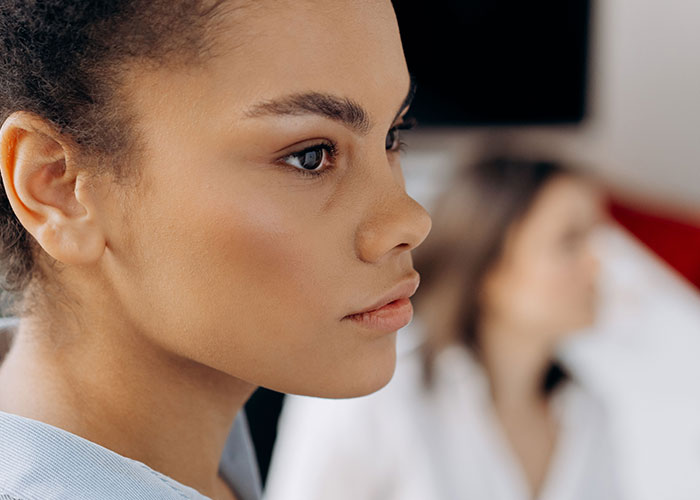 A woman in profile, with a blurred figure in the background, contemplating horrible things committed by close friends that broke people's trust.