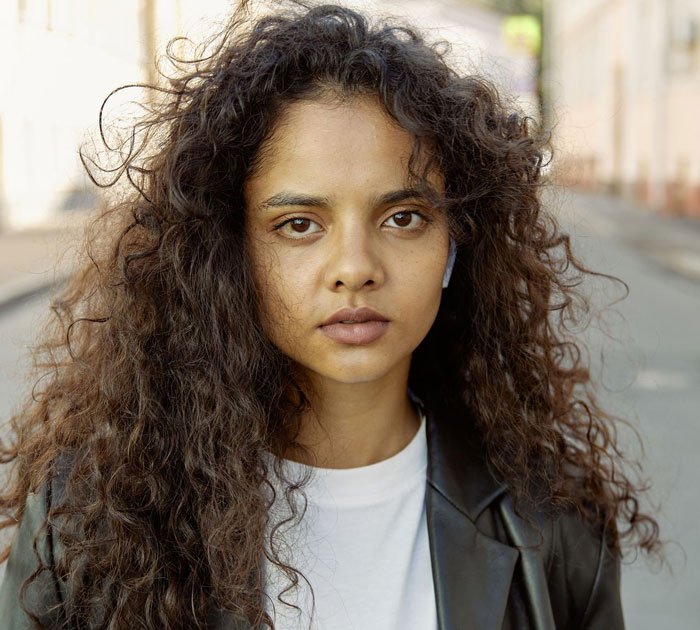 A young woman with curly hair looking directly at the camera, thinking about her job being on the line.