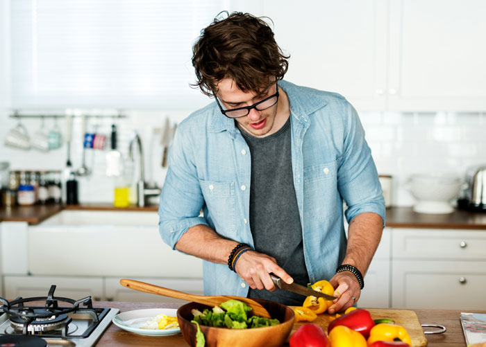 A husband cooking in the kitchen, representing his frustration over his wife's gaming problem affecting their son.