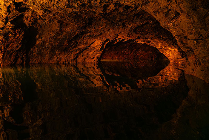 Dark underground cave with water reflecting rocky walls in terrifying scene