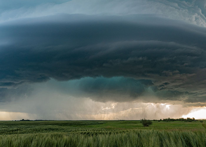 Dark storm clouds over green field signaling time to leave immediately