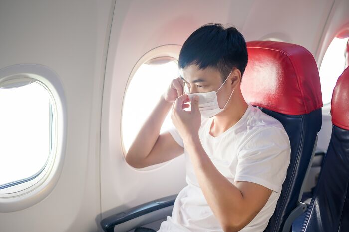 A man adjusts his mask on a plane, showing a common plane interaction.