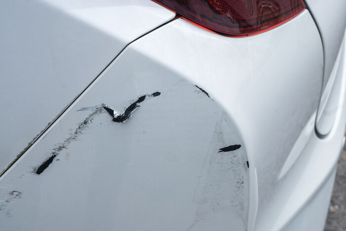 Scratches and damage on the white bumper of a car, representing disturbing things about friends.