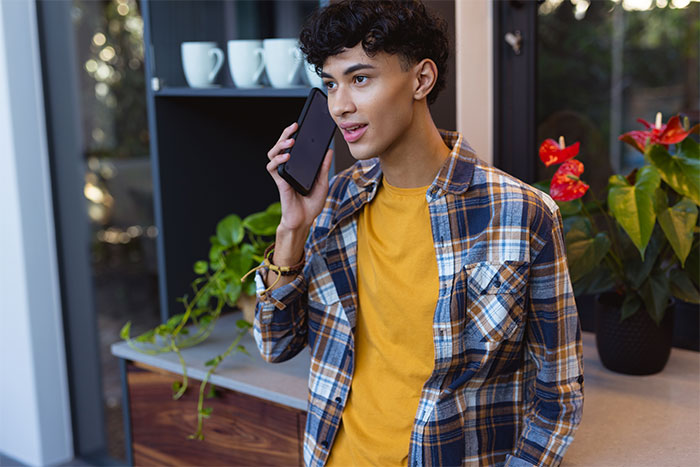 A young man on a phone call in a modern kitchen, talking about a woman being told to leave home.