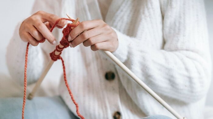 Person knitting red yarn with needles, mind-bending dilemmas hands close-up