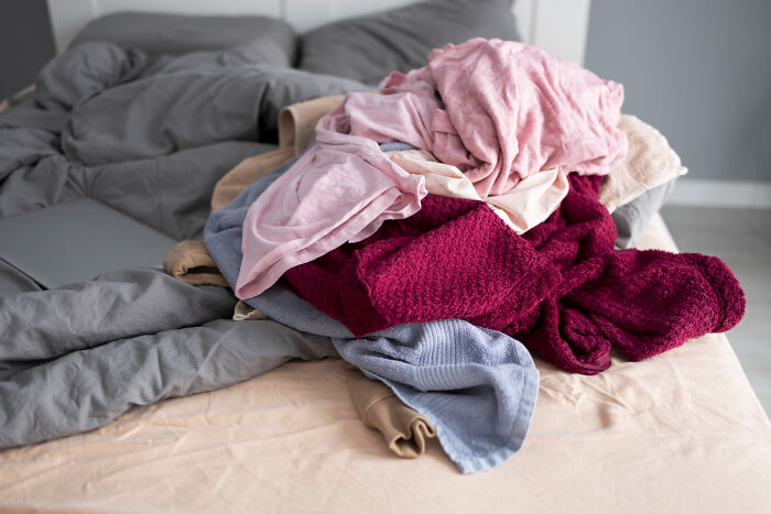 A pile of clothes on an unmade bed, representing disturbing things people learn about friends and seeing them differently.