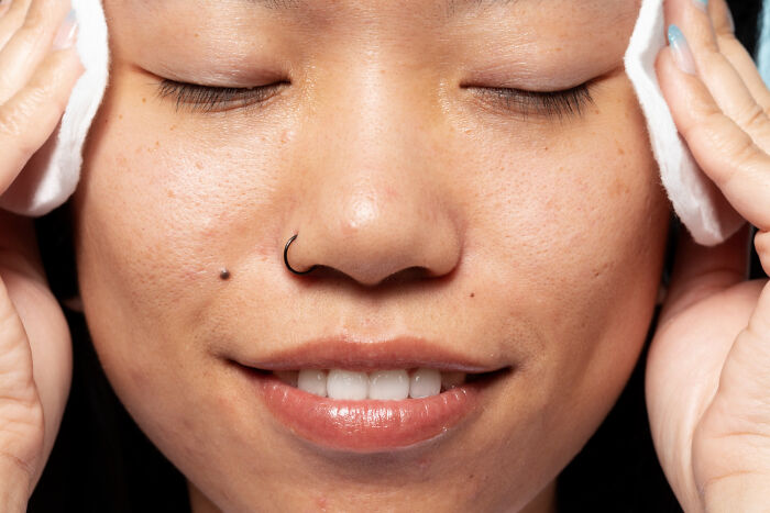Person cleansing face with cotton pads, highlighting skin care and human body