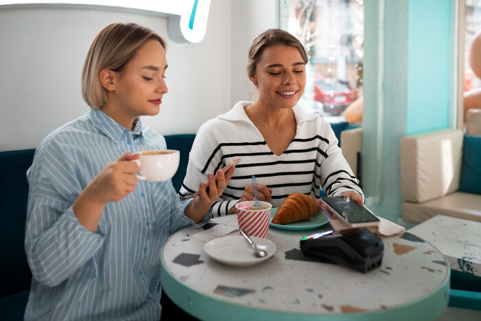 Women using mobile payment to pay in cafe with coffee and croissant