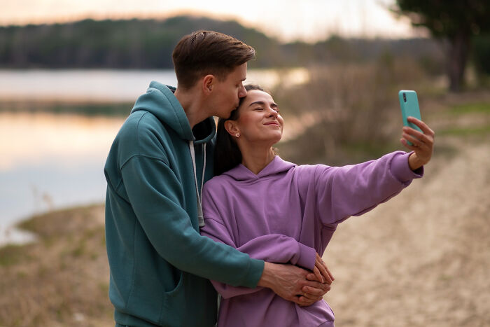 Couple taking selfie outdoors by the lake at sunset