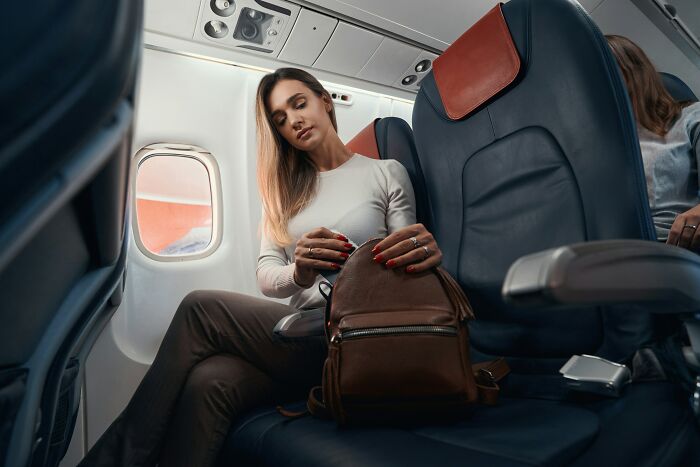 A woman with blonde hair adjusting her bag while sitting in a plane, showcasing typical plane interactions.