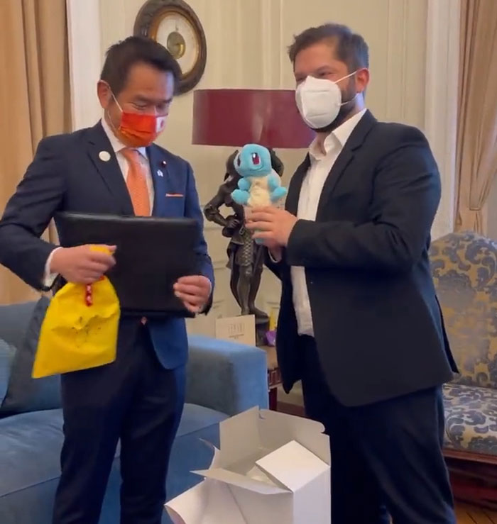 World leaders exchanging gifts and smiling indoors while wearing masks