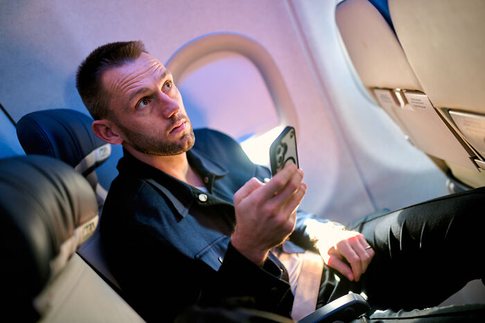 A man looking up with his phone in hand inside a plane, depicting a moment of plane interactions.