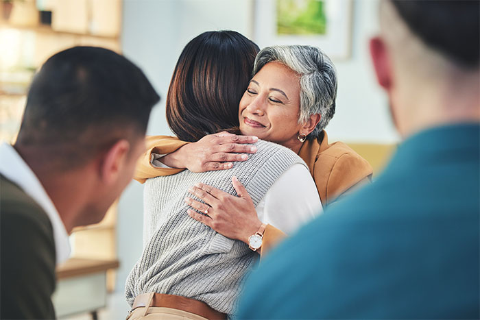An older woman with grey hair smiles while hugging a younger woman, representing a woman told to leave home refusing to follow one rule.