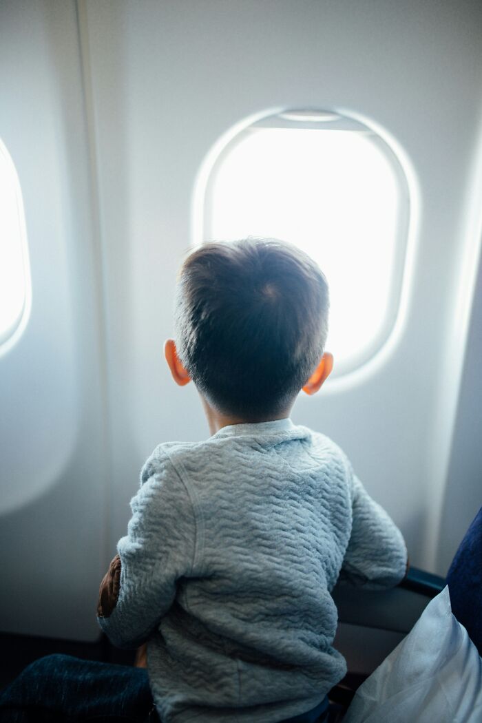 A young child looking out a plane window, experiencing plane interactions during travel.