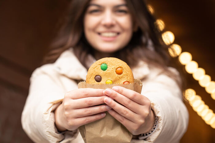 A smiling woman offering a cookie, a contrast to disturbing things people learned about their friends.