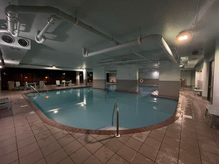 A deserted indoor swimming pool area with dim lighting, creating an eerie liminal space.