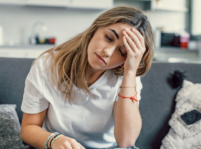 Stressed woman sitting on couch with head in hand Stressed woman sitting on couch with head in hand