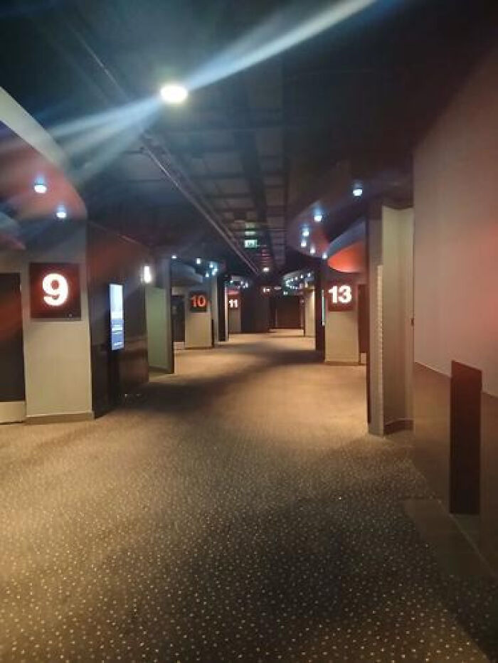 An empty, dimly lit movie theater hallway with numbered doors, a haunting liminal space.