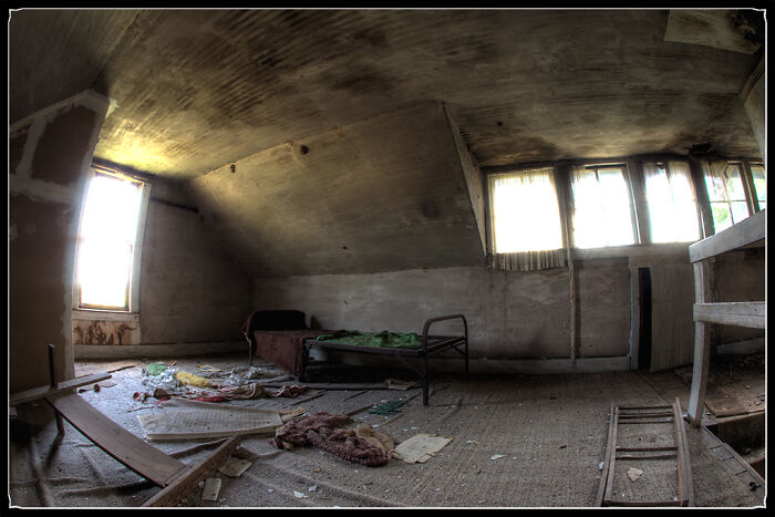 Interior of creepy abandoned room with broken bed and scattered debris