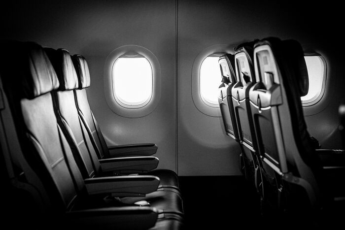 Empty plane seats next to windows in a dimly lit cabin, capturing plane interactions.