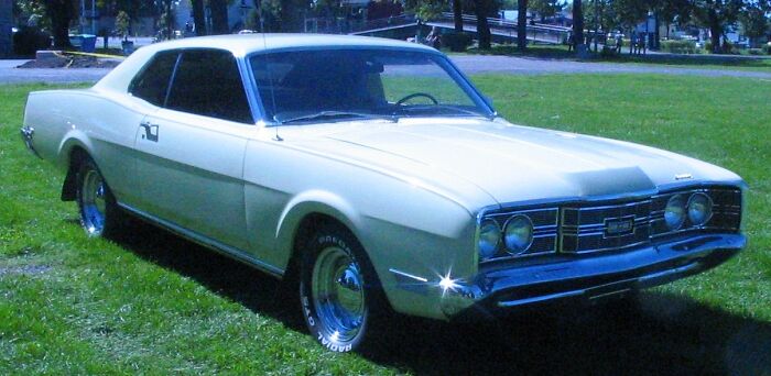 A vintage cream-colored car parked on green grass, representing an unsolved mystery of classic automobiles.