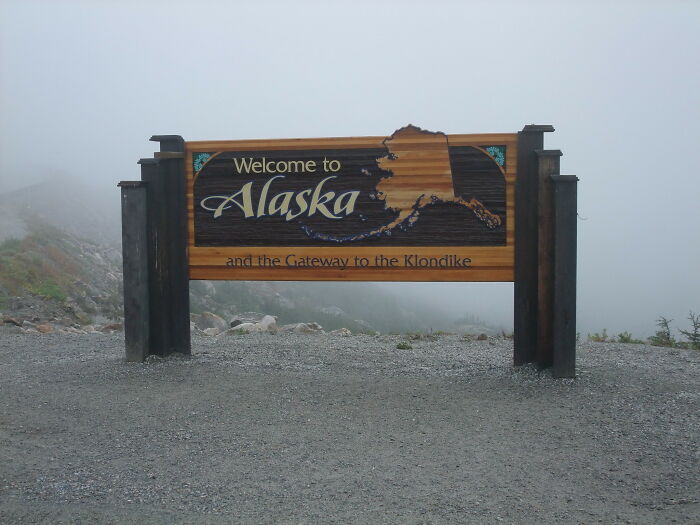 A wooden welcome to Alaska sign with The Gateway to the Klondike in a misty landscape, one of the crazy facts.
