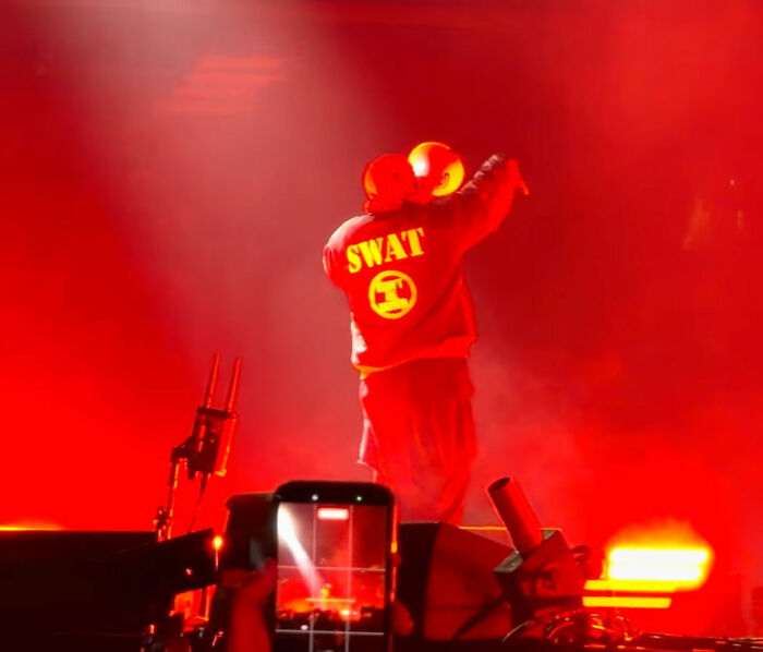 Rihanna's partner on stage in a red SWAT sweatshirt, holding a microphone. The stage is bathed in red light.
