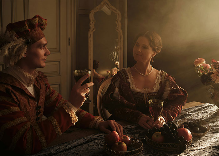 Couple in vintage clothing sharing wine at a fruit-adorned table in historic setting Couple in vintage clothing sharing wine at a fruit-adorned table in historic setting