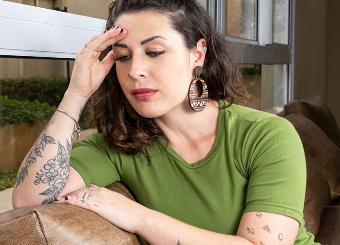 Worried woman sitting on sofa with tattooed arms and large earrings