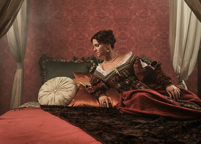 Woman in vintage dress reclining on luxurious bed with red and gold decor Woman in vintage dress reclining on luxurious bed with red and gold decor