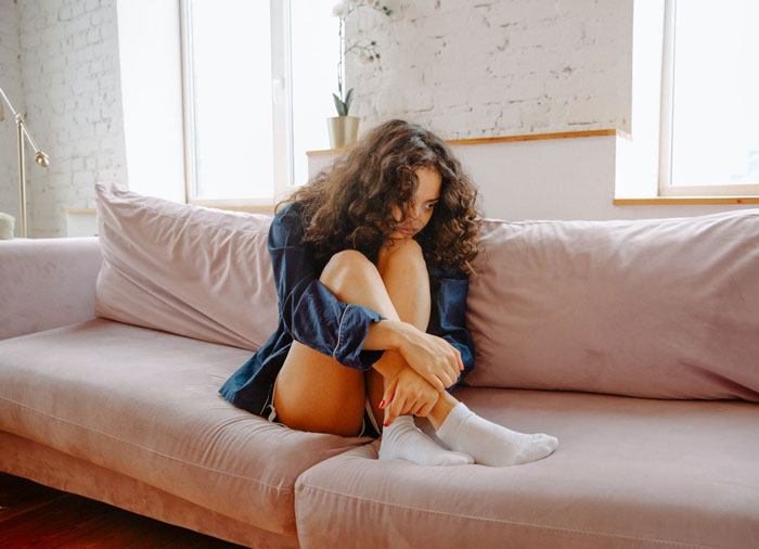 A woman with messy hair, told her job might be on the line, sits on a couch, looking worried.