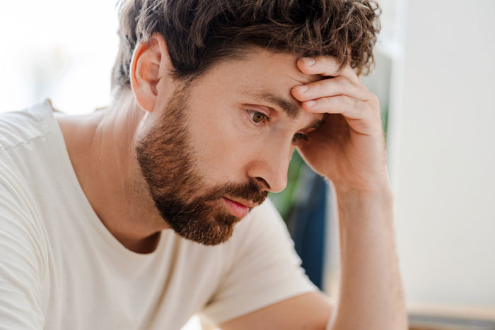A man with a beard and short curly hair, looking stressed, holding his head in his hand due to gaming problem.