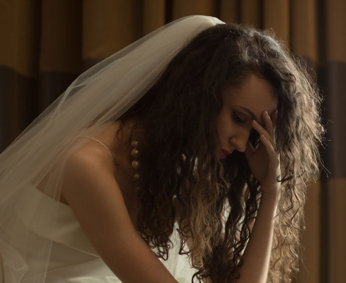 A distressed bride with a veil, holding her head, looking upset during her wedding due to her cousin's actions. A distressed bride with a veil, holding her head, looking upset during her wedding due to her cousin's actions.