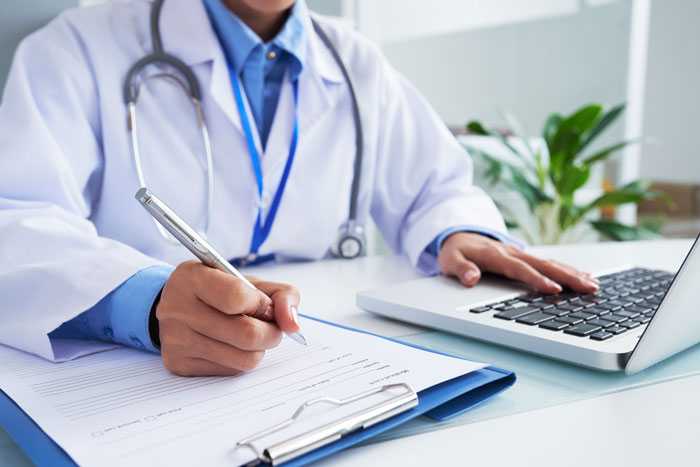 Healthcare professional writing notes and using laptop