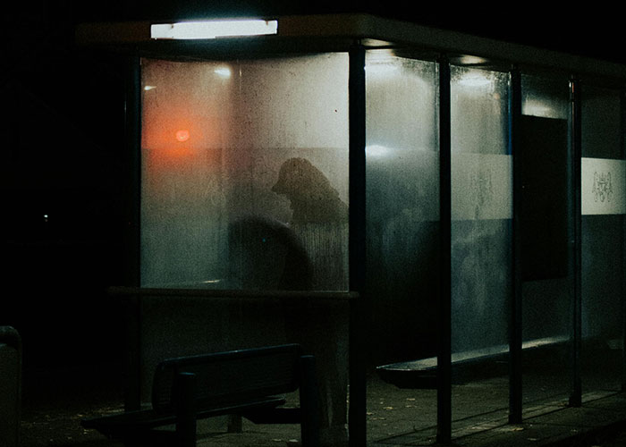 Silhouetted figure sitting in dimly lit enclosed bus stop at night